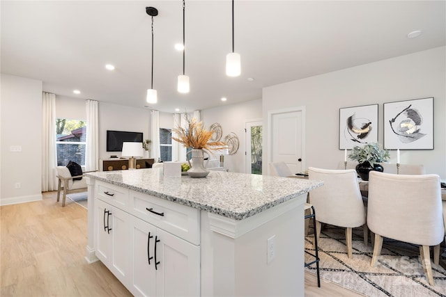 kitchen with a kitchen island, pendant lighting, light hardwood / wood-style flooring, light stone countertops, and white cabinets