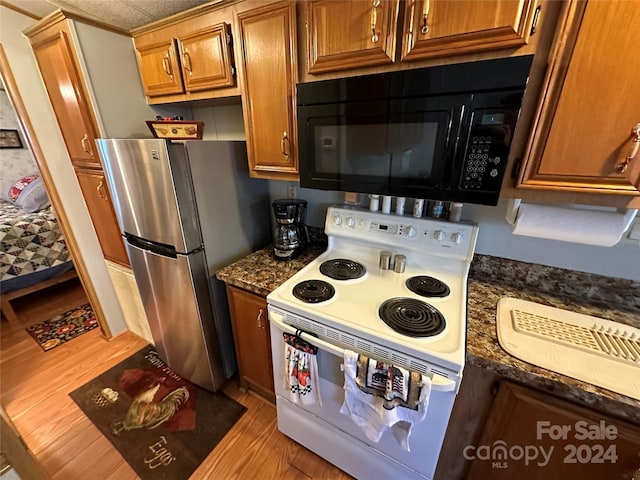 kitchen featuring white electric range oven, light hardwood / wood-style flooring, stainless steel refrigerator, and dark stone counters