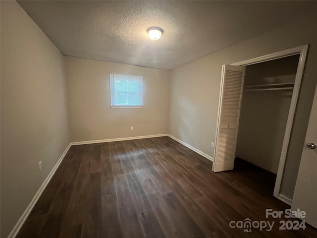 unfurnished bedroom with dark wood-type flooring, a textured ceiling, and a closet