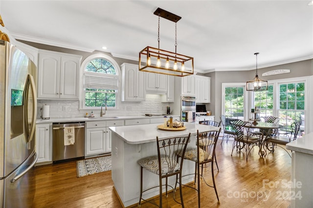 kitchen with pendant lighting, appliances with stainless steel finishes, a kitchen island, white cabinetry, and sink