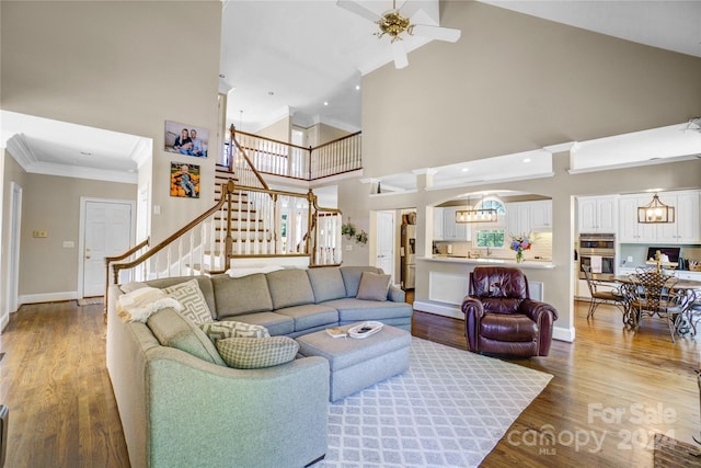 living room with ornamental molding, ceiling fan with notable chandelier, high vaulted ceiling, and hardwood / wood-style floors