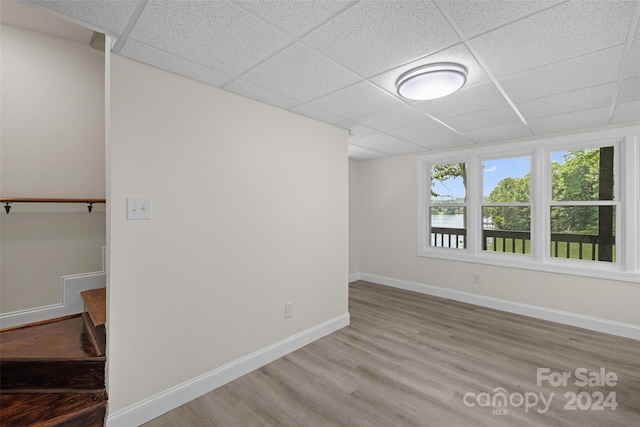 unfurnished room with a water view, a drop ceiling, and light wood-type flooring