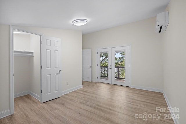 unfurnished room featuring a wall unit AC, french doors, and light wood-type flooring