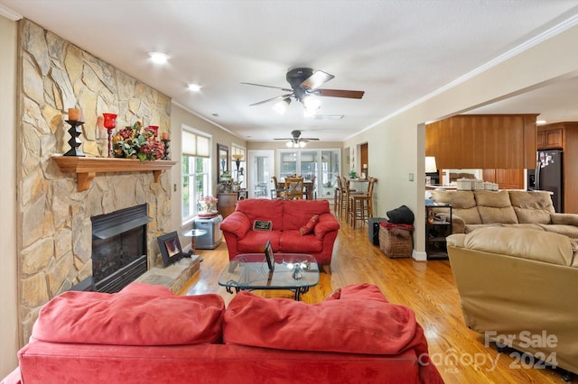 living room with a stone fireplace, ceiling fan, ornamental molding, and light wood-type flooring