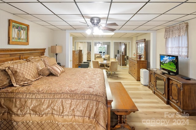 bedroom with ceiling fan, a drop ceiling, and light wood-type flooring