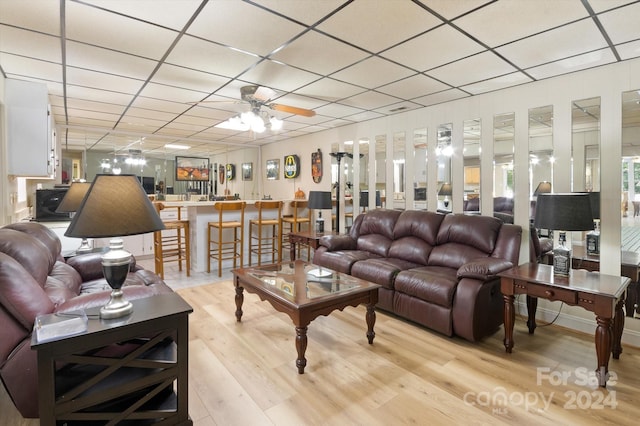 living room featuring a drop ceiling, ceiling fan, and light wood-type flooring