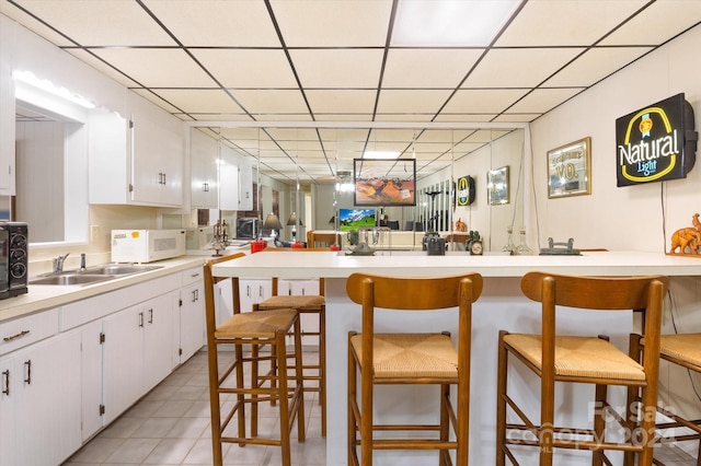 kitchen featuring a drop ceiling, white cabinetry, and a breakfast bar area