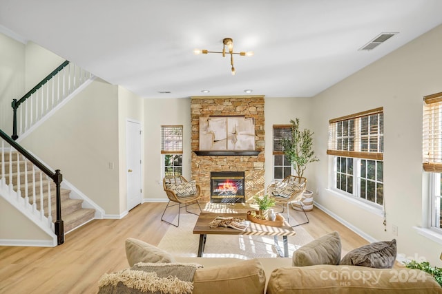 living room featuring light hardwood / wood-style floors, a stone fireplace, and an inviting chandelier