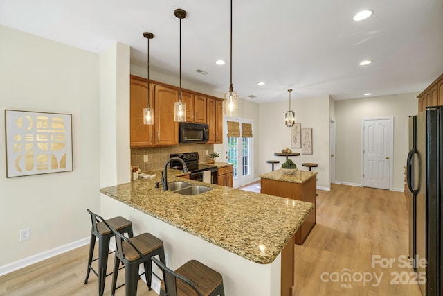 kitchen featuring decorative backsplash, a center island, a peninsula, black appliances, and a sink