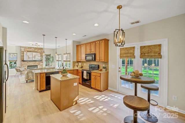 kitchen featuring visible vents, a peninsula, light stone countertops, black appliances, and backsplash