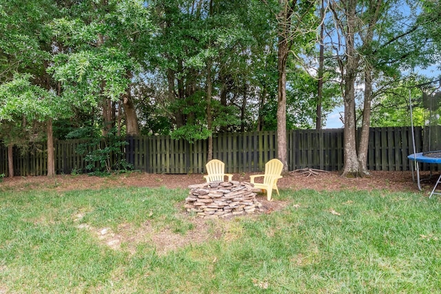 view of yard with a fenced backyard, a trampoline, and a fire pit