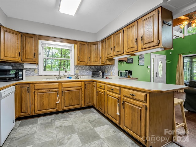 kitchen featuring a kitchen bar, kitchen peninsula, dishwasher, a wealth of natural light, and sink