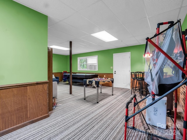 rec room featuring a drop ceiling, carpet, wood walls, and cooling unit