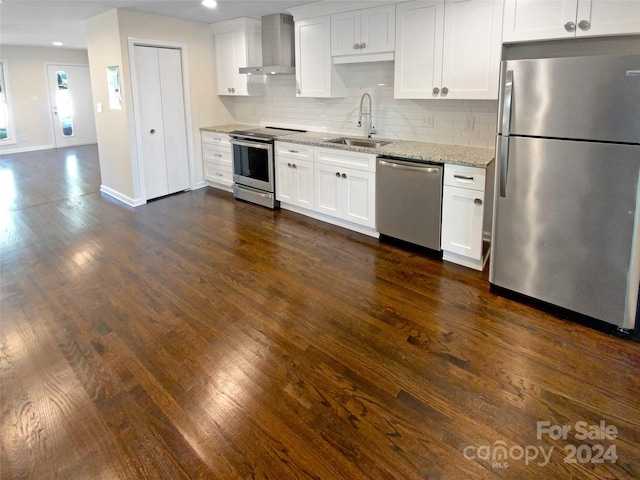 kitchen with stainless steel appliances, wall chimney range hood, white cabinets, light stone counters, and sink