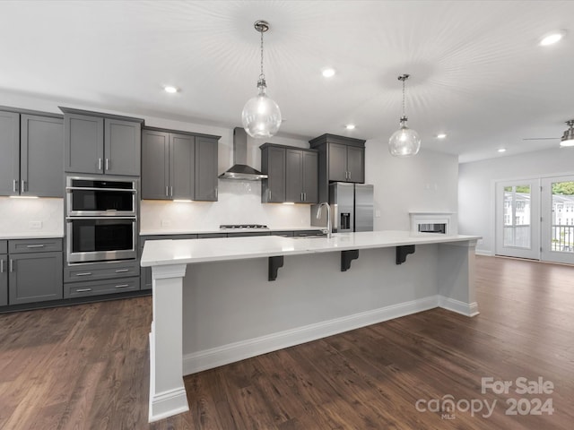 kitchen featuring a kitchen island with sink, wall chimney range hood, and appliances with stainless steel finishes