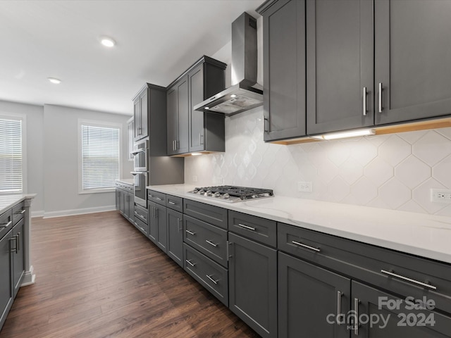 kitchen with gray cabinetry, dark hardwood / wood-style floors, stainless steel appliances, and wall chimney range hood