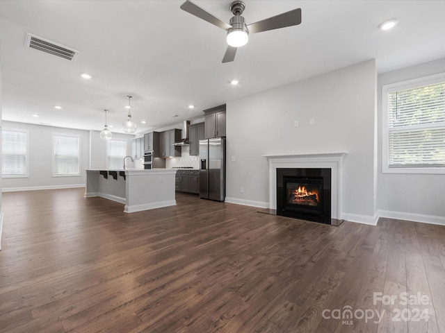 unfurnished living room featuring sink, a wealth of natural light, dark wood-type flooring, and ceiling fan