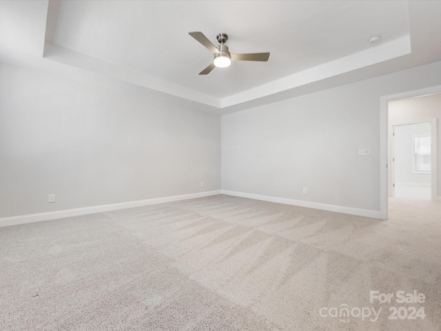 empty room featuring carpet flooring, a raised ceiling, and ceiling fan