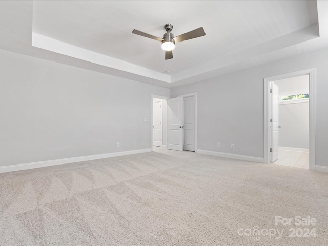 unfurnished room with ceiling fan, a raised ceiling, and light colored carpet