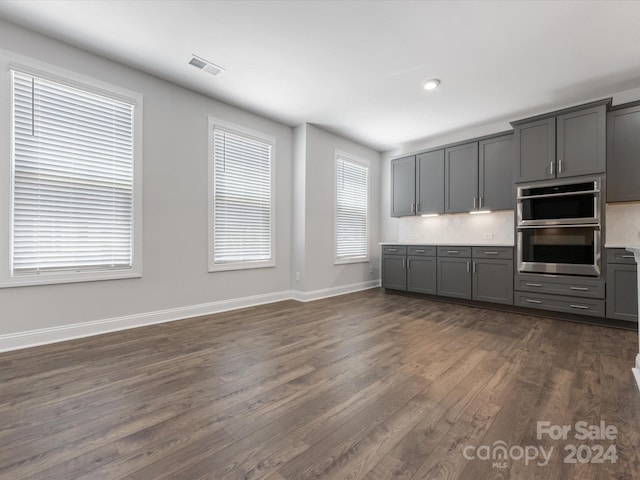 kitchen with gray cabinets, decorative backsplash, dark hardwood / wood-style flooring, and stainless steel double oven