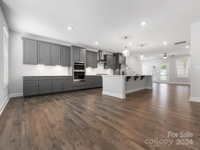 kitchen with gray cabinetry, a kitchen island with sink, wall chimney range hood, stainless steel refrigerator with ice dispenser, and decorative light fixtures