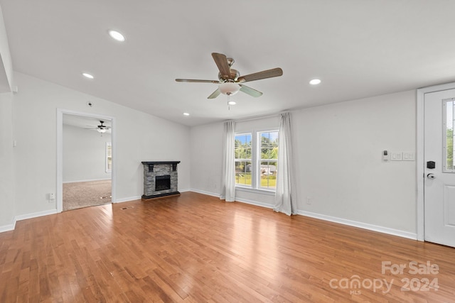 unfurnished living room with ceiling fan, a stone fireplace, and light wood-type flooring