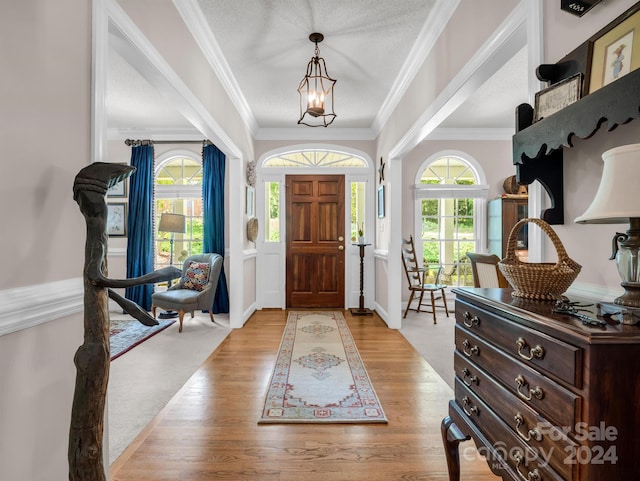 foyer with a textured ceiling, ornamental molding, a chandelier, and light wood-type flooring