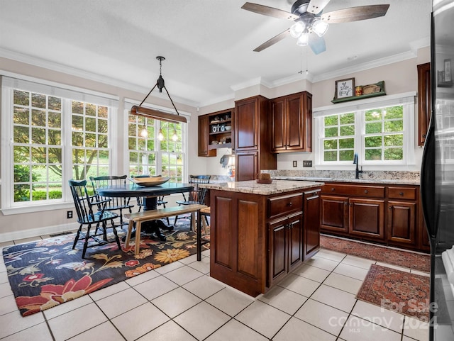 kitchen with a kitchen island, decorative light fixtures, ornamental molding, light stone counters, and dark brown cabinets