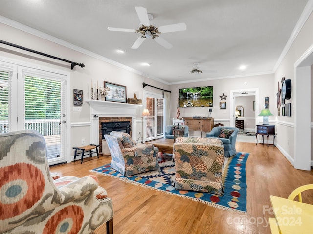 living room with a brick fireplace, light hardwood / wood-style flooring, crown molding, and ceiling fan