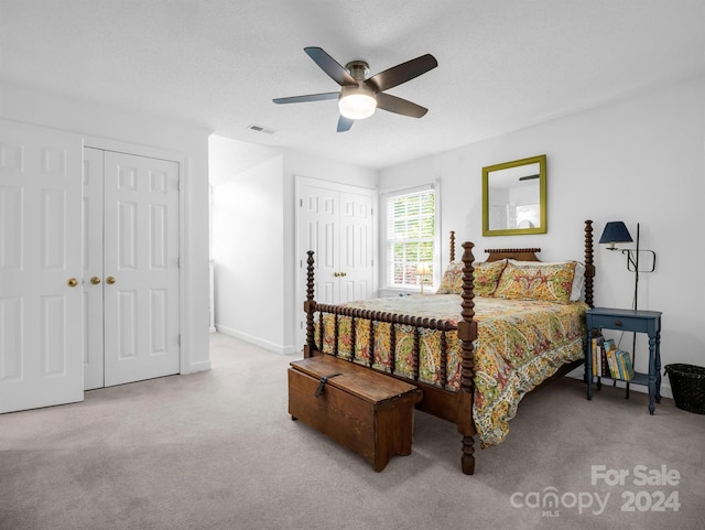 bedroom featuring ceiling fan, light colored carpet, multiple closets, and a textured ceiling