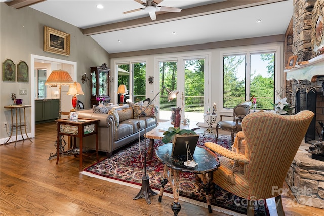 living room with a stone fireplace, ceiling fan, wood-type flooring, and lofted ceiling with beams