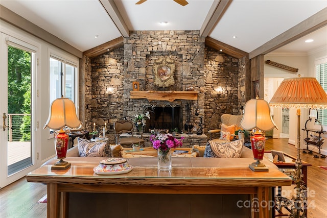 living room with lofted ceiling with beams, light hardwood / wood-style floors, a stone fireplace, and ceiling fan