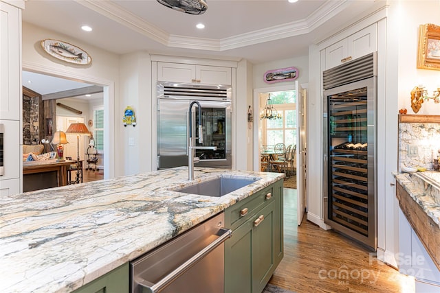 kitchen with stainless steel appliances, a raised ceiling, green cabinets, wine cooler, and light wood-type flooring