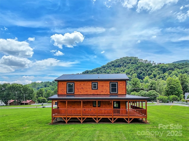 rear view of property with a wooded view, metal roof, faux log siding, and a lawn