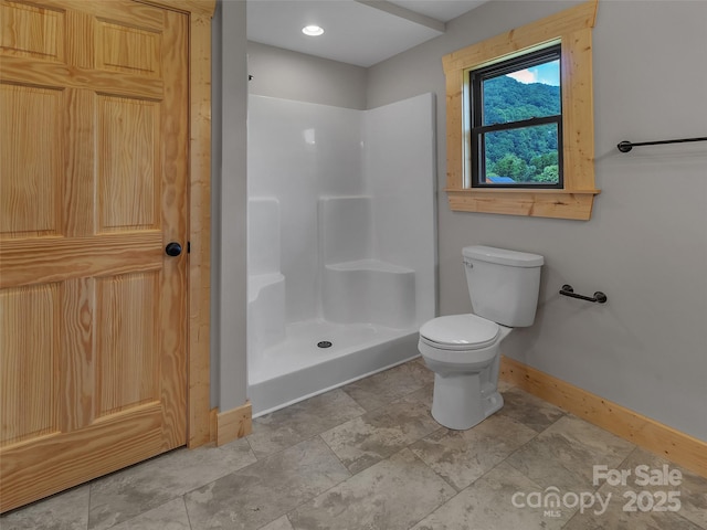 bathroom with toilet, baseboards, and a stall shower