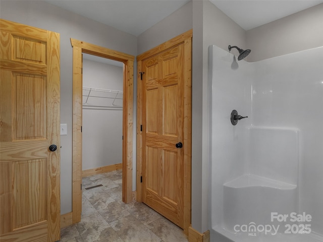 bathroom featuring a shower, baseboards, a spacious closet, and visible vents