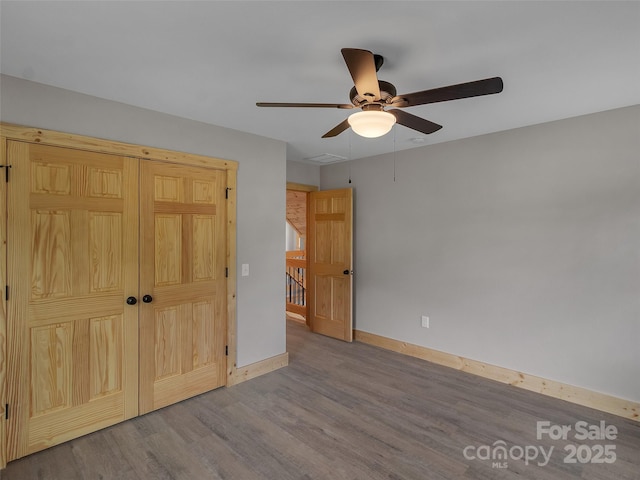 unfurnished bedroom featuring ceiling fan, a closet, visible vents, wood finished floors, and baseboards
