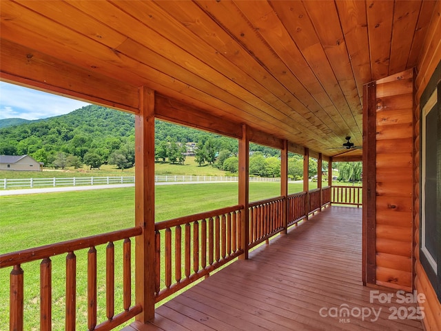 deck with a wooded view, a yard, fence, and a mountain view