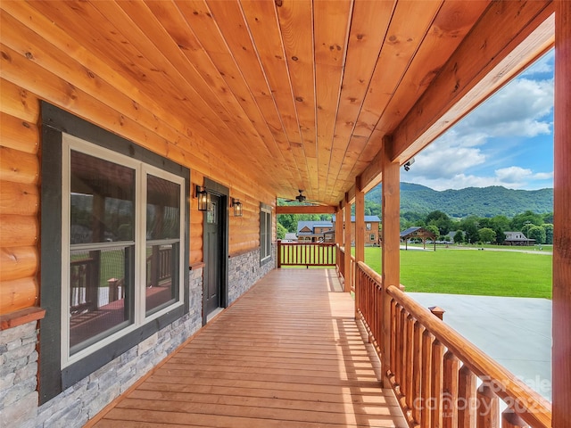 wooden deck with a yard, a porch, a mountain view, and ceiling fan