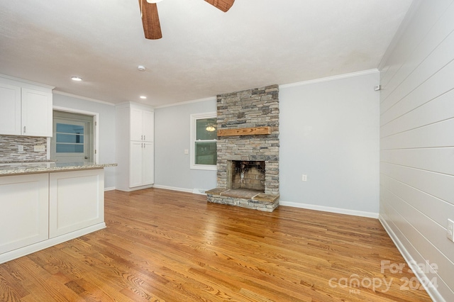 unfurnished living room with a stone fireplace, crown molding, and light wood-type flooring