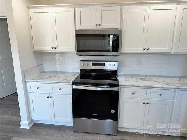 kitchen with light wood-style flooring, white cabinets, appliances with stainless steel finishes, decorative backsplash, and light stone countertops