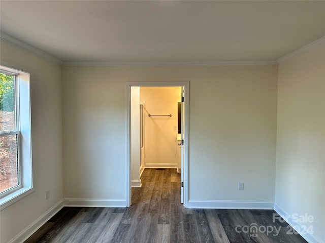 empty room featuring ornamental molding, dark wood-type flooring, and baseboards