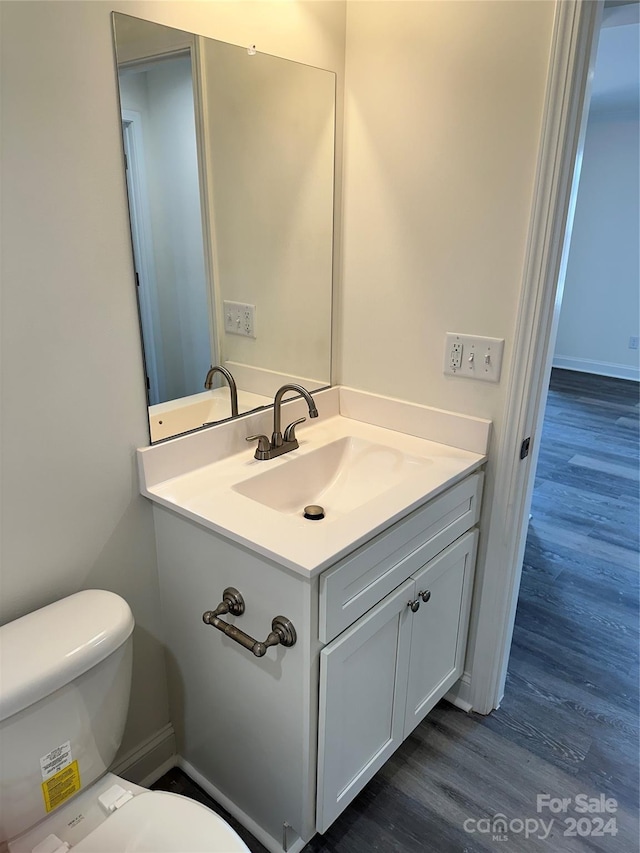 half bath featuring toilet, wood finished floors, and vanity