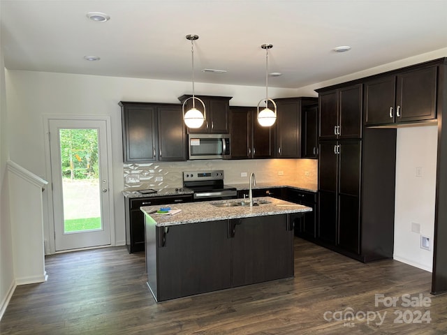 kitchen with light stone countertops, stainless steel appliances, sink, decorative light fixtures, and an island with sink