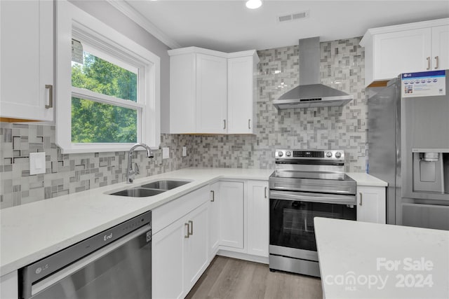 kitchen with stainless steel appliances, wall chimney exhaust hood, white cabinets, and sink