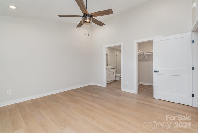 unfurnished bedroom with connected bathroom, a spacious closet, ceiling fan, light hardwood / wood-style floors, and a closet