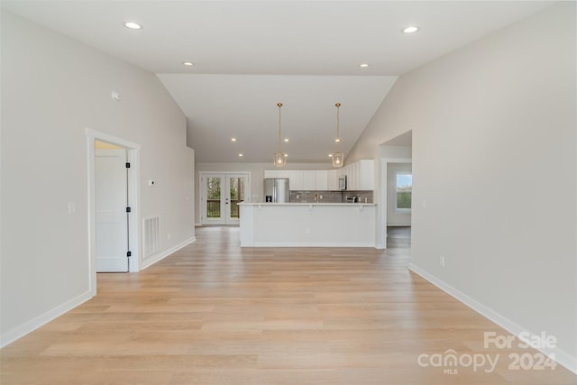 unfurnished living room with french doors, light hardwood / wood-style floors, and lofted ceiling