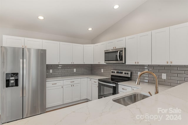 kitchen with light stone countertops, stainless steel appliances, vaulted ceiling, sink, and white cabinets