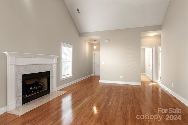 unfurnished living room with light hardwood / wood-style flooring, a premium fireplace, and high vaulted ceiling