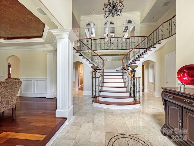 foyer with decorative columns, a towering ceiling, ornamental molding, and an inviting chandelier